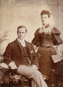 Sepia-tone photo of a seated man and standing woman, 1895