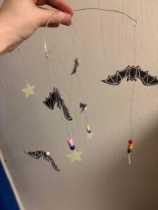 Two-dimensional black bats, yellow stars, and colorful beads hang from nearly transparent fishing line and a silver wire cross-piece as a mobile