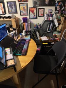 Laptop with a secondary monitor, external keyboard, and mouse, with hexagonal bookshelf in the background and art on the wall.